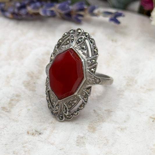 Silver ring with a red stone on a textured surface with flowers in the background