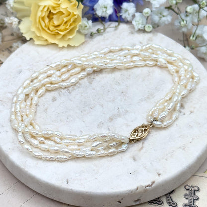 Pearl necklace with a gold clasp on a marble surface with flowers in the background