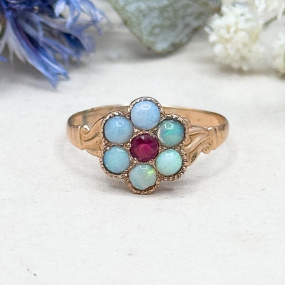 Ring with blue and red gemstones on a white surface with flowers in the background