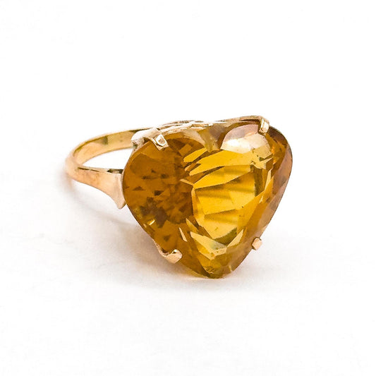 Gold ring with a large heart-shaped yellow gemstone on a white background