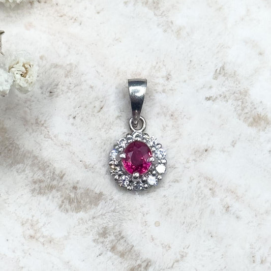 Silver pendant with a red gemstone on a white textured surface with flowers.