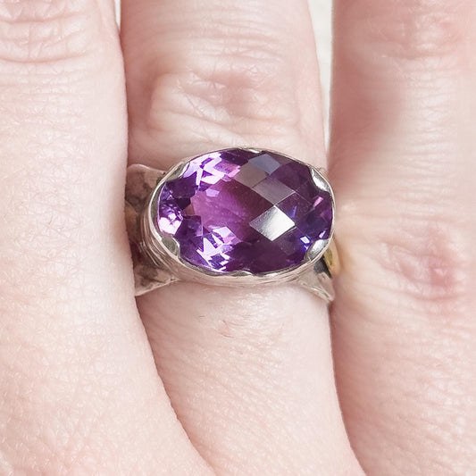 Silver ring with a purple gemstone on a hand against a neutral background