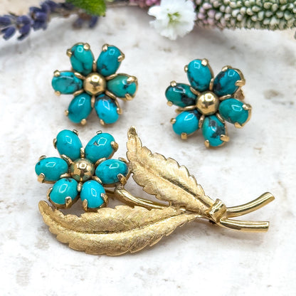 Gold and turquoise jewelry set on a textured surface with flowers in the background