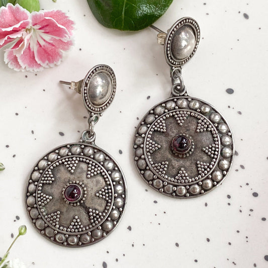 Pair of silver earrings with gemstones on a white background with flowers and leaves.