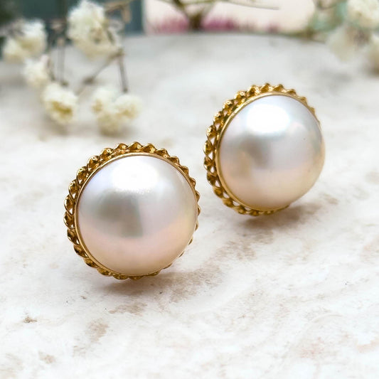 Pearl earrings with gold accents on a light surface with blurred flowers in the background