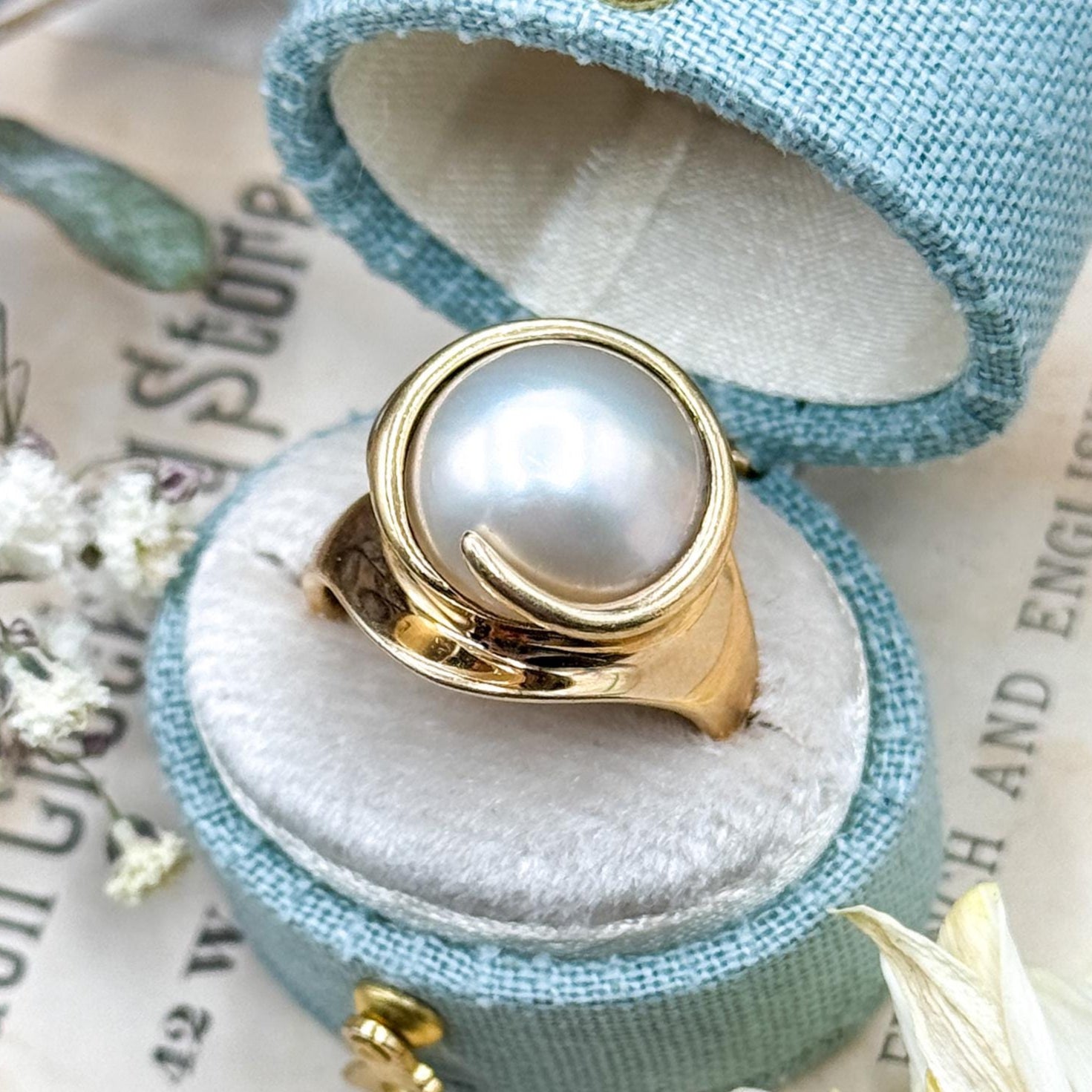 Gold ring with a pearl in a light blue jewelry box on a newspaper background