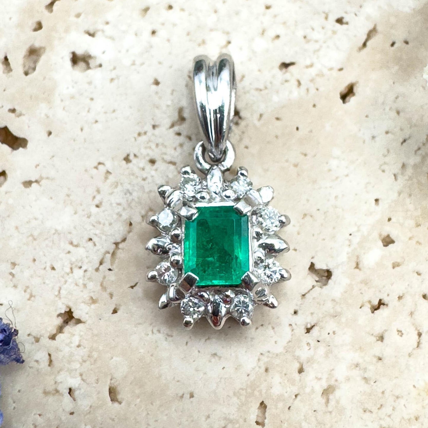 Silver pendant with a green gemstone on a textured beige surface with flowers.