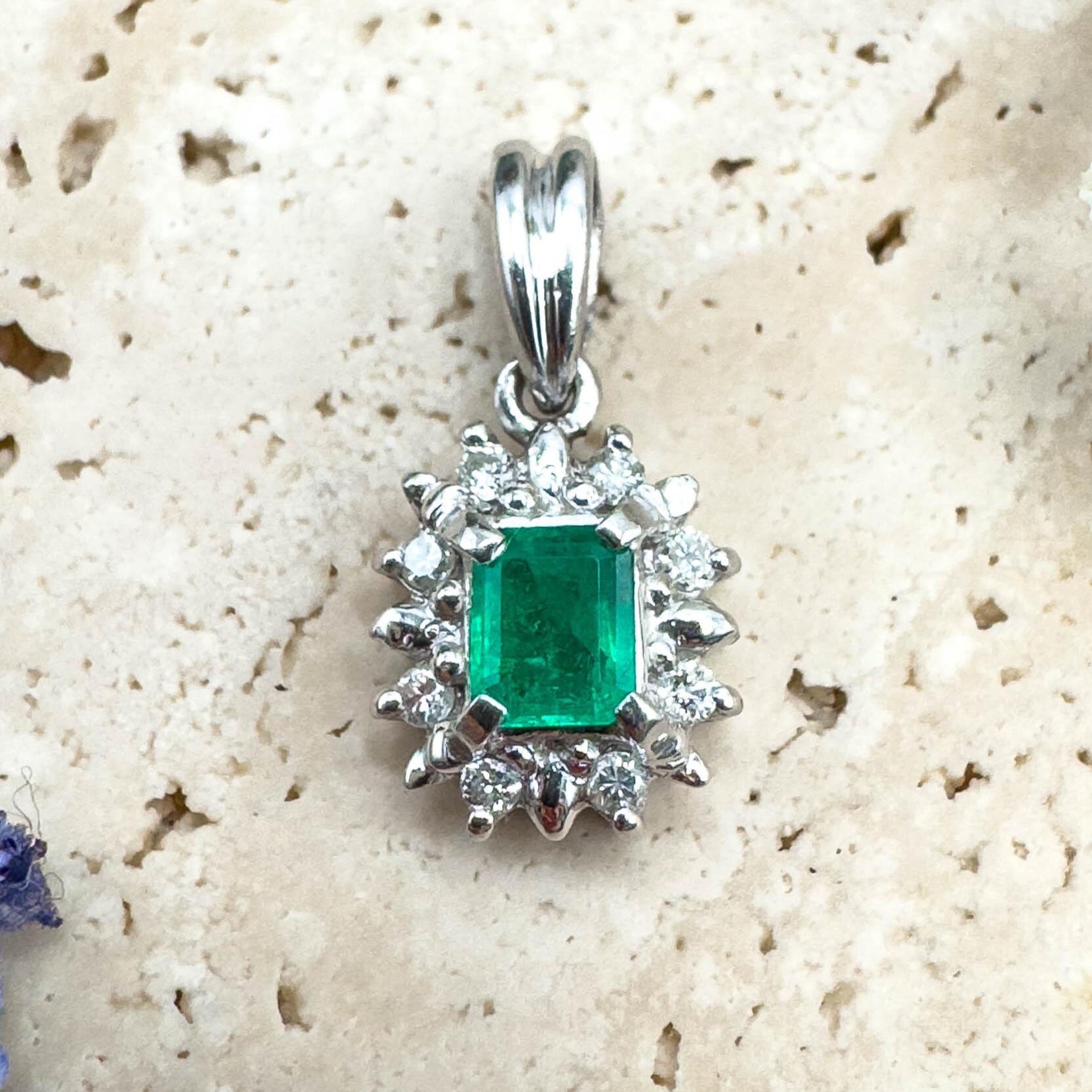 Silver pendant with a green gemstone on a textured beige surface with flowers.