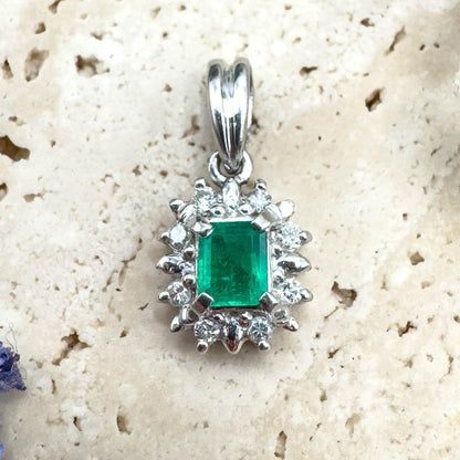 Silver pendant with a green gemstone on a textured beige surface with flowers.