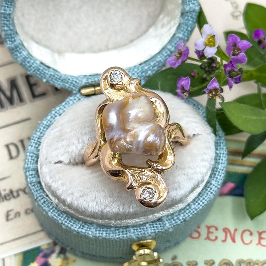 Gold turtle-shaped pendant with a pearl on a blue cushioned stand, surrounded by greenery and text.