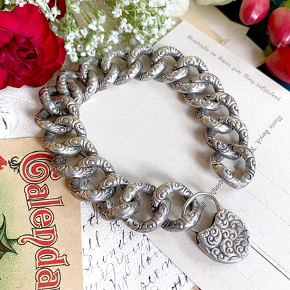 Silver bracelet with a heart charm on a surface with flowers and a calendar.