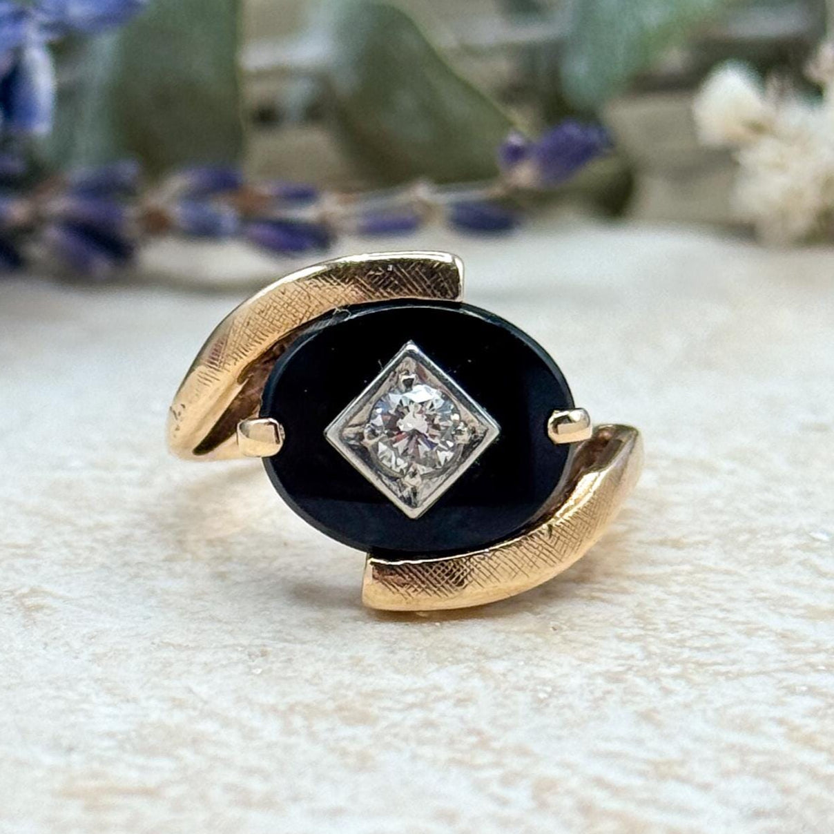 Gold ring with a black stone and diamond-like center on a textured surface.