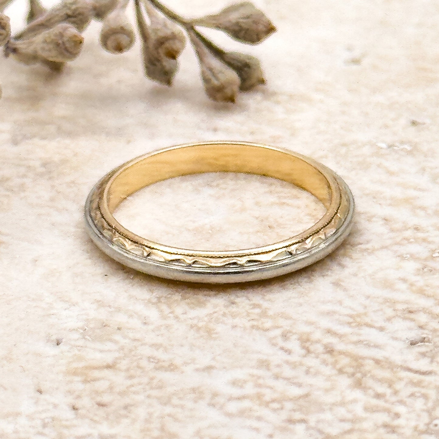 Gold ring on a textured beige surface with dried flowers.
