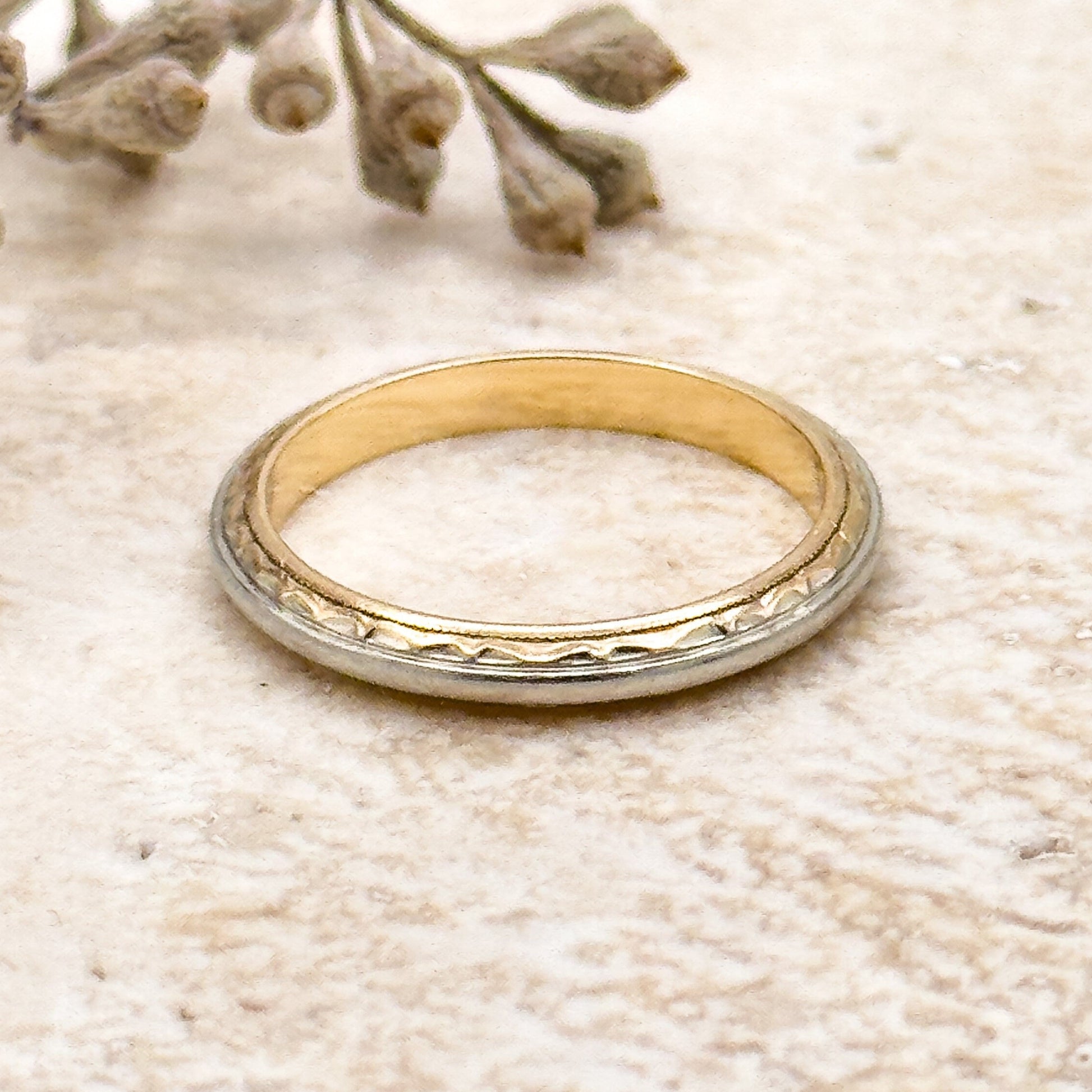 Gold ring on a textured beige surface with dried flowers.
