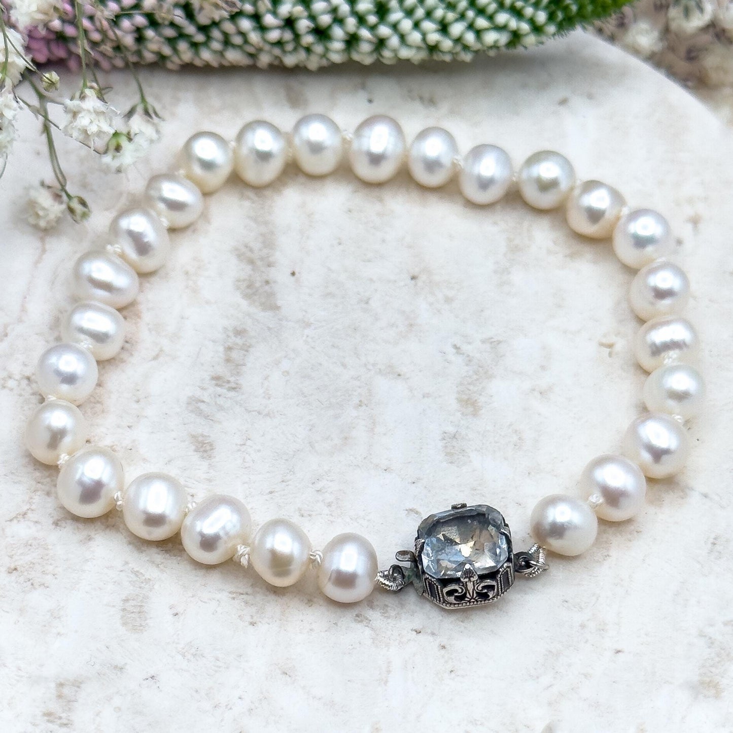 Pearl bracelet with a silver clasp on a textured surface with flowers in the background
