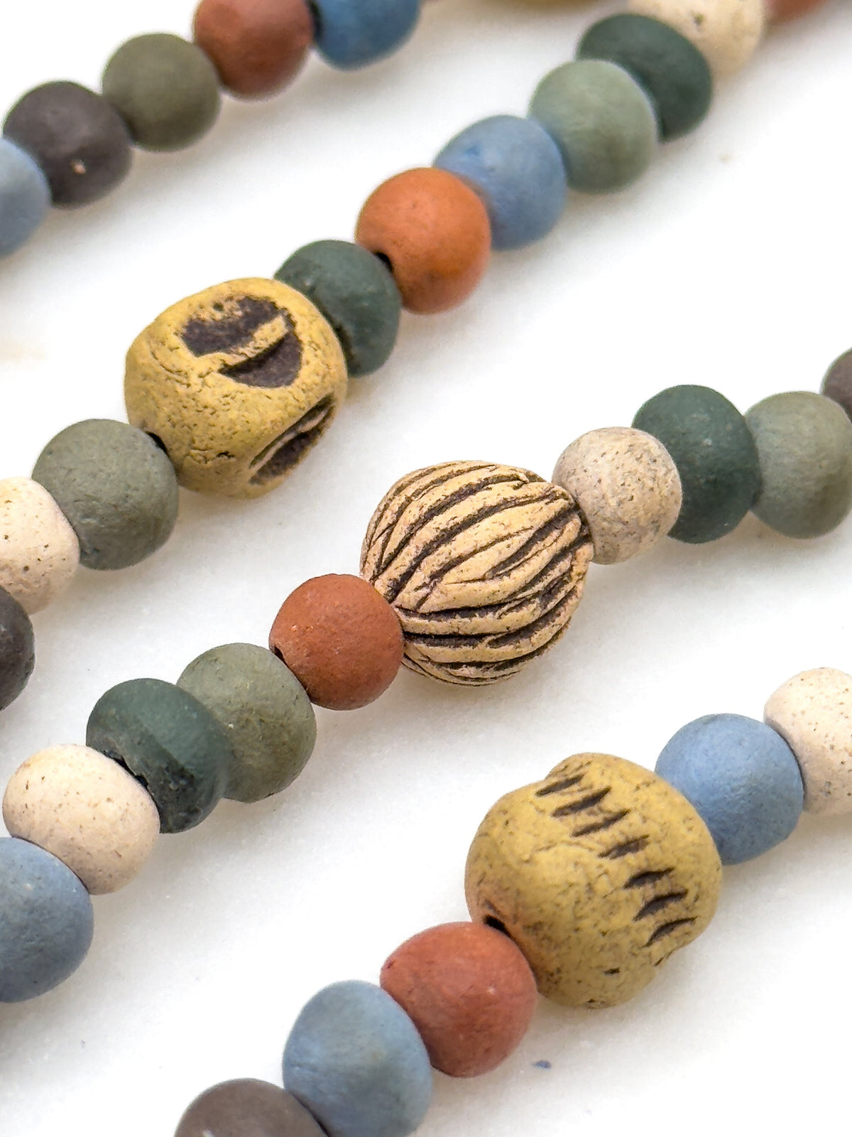 Three strand sections lying diagonally side by side, cropped close enough to see the drilled holes and the incised lines cut into the larger cream and ochre beads.