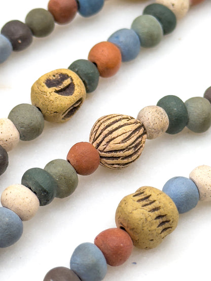 Three strand sections lying diagonally side by side, cropped close enough to see the drilled holes and the incised lines cut into the larger cream and ochre beads.