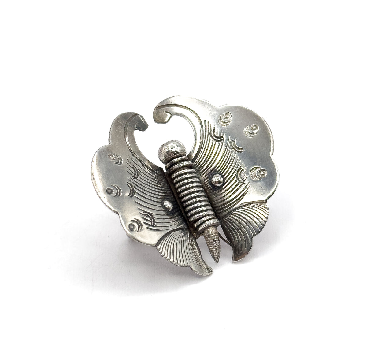A single sterling silver butterfly brooch shown face-up on a white background, its curled upper wings and finely etched lines flanking a ribbed, tapering body.