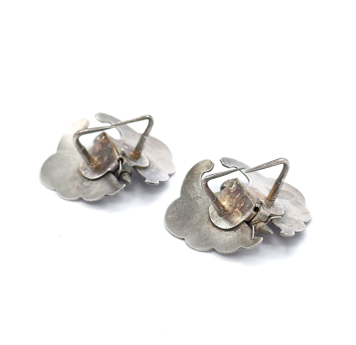 Angled three-quarter view of both reverses, where the wire leg-shaped clips stand proud of the bodies and the scalloped wing edges catch the light.