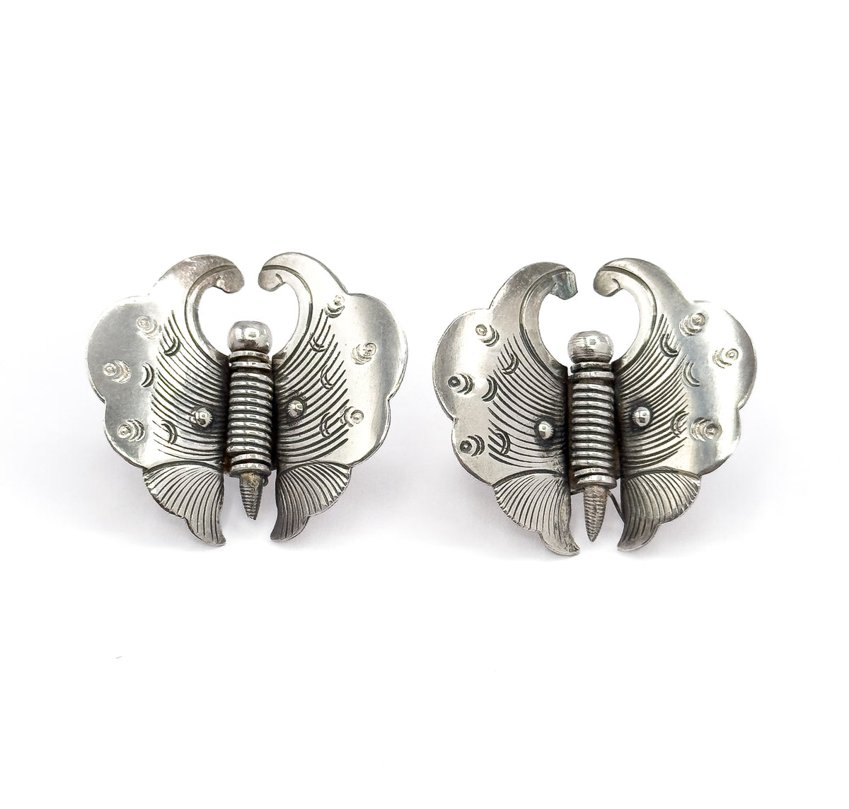 Front view of the pair side by side, showing the etched, scalloped wings with dotted and curved markings, curled antennae and ribbed bodies tapering to a point, patina in the recesses.