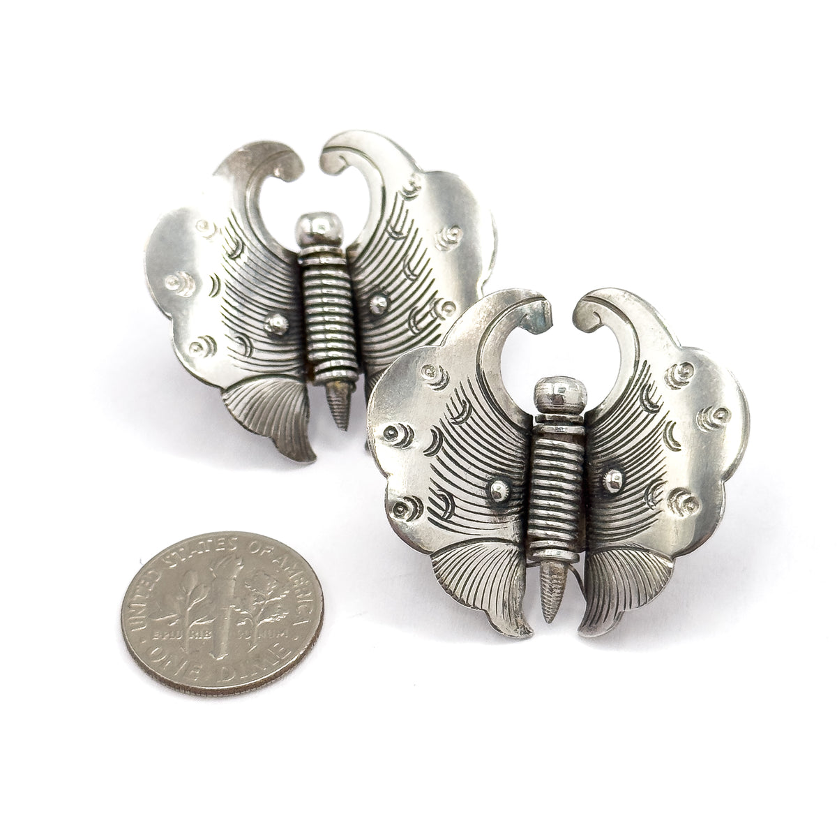 The pair shown front-up beside a dime for scale, each butterfly brooch roughly the width of the coin and a half, with curled antennae and etched, scalloped wings.