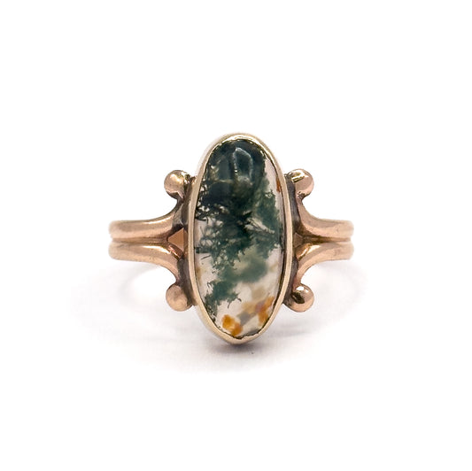 Face-on again but further back, showing the full ring upright with the moss agate's green and rust markings, the scrolled shoulders, and the two slim bands of the split shank curving down.